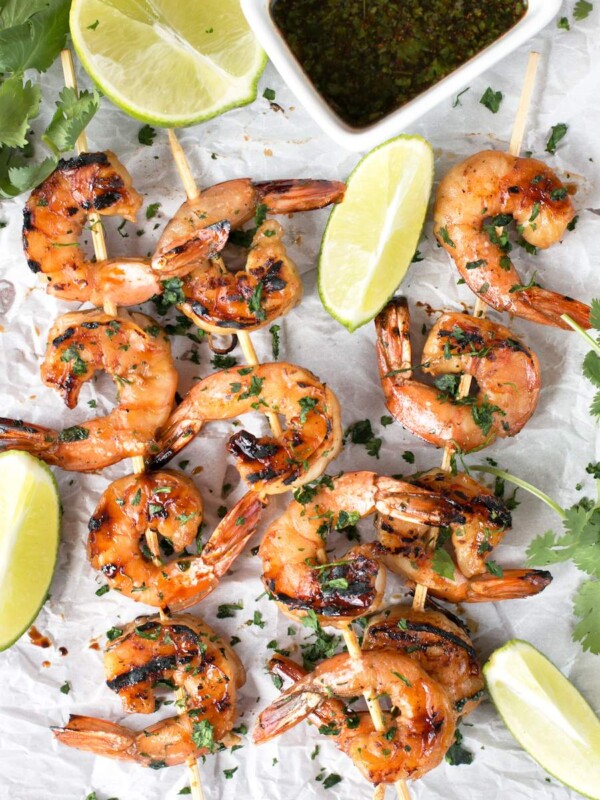 Agave Cilantro Shrimp Skewers with dipping sauce and lime on parchment paper.