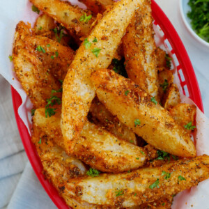 Top down view of crispy potato wedges in a red basket.