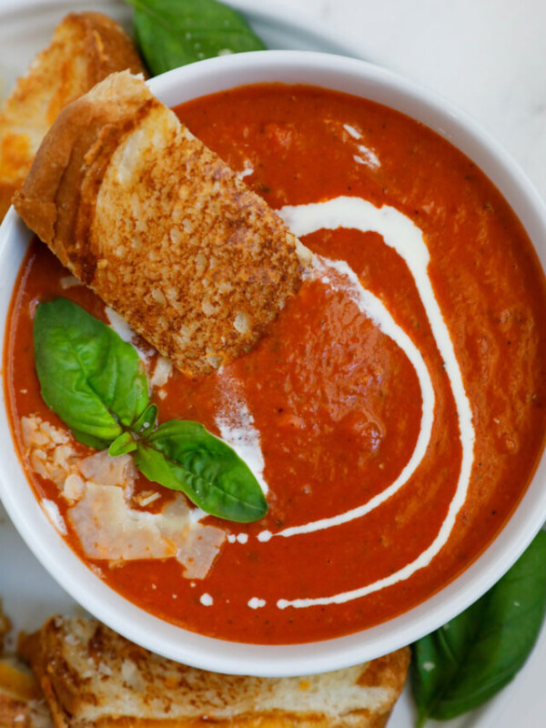 Bowl of tomato soup with bread, basil, and parmesan on top.