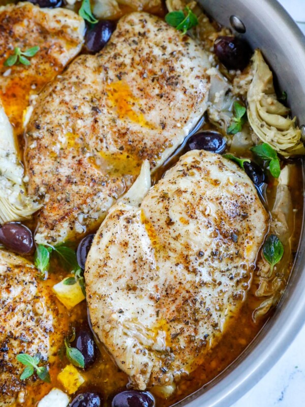 Overhead shot of greek chicken in a skillet with olives and artichokes.