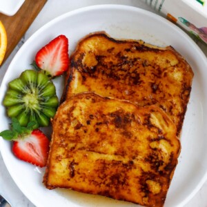 Orange french toast on a plate served with a kiwi and sliced strawberry.