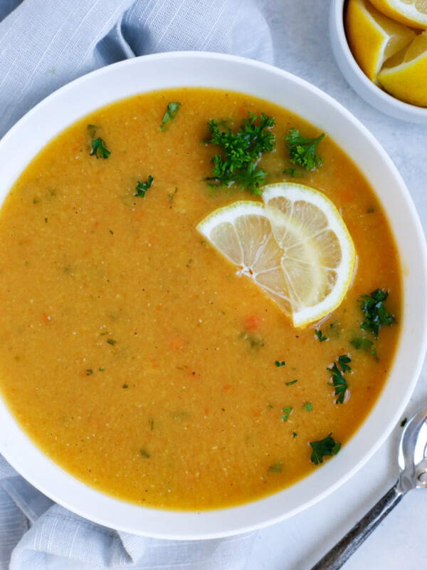 Lebanese lentil soup served in a white bowl and garnished with lemon wedges and parsley