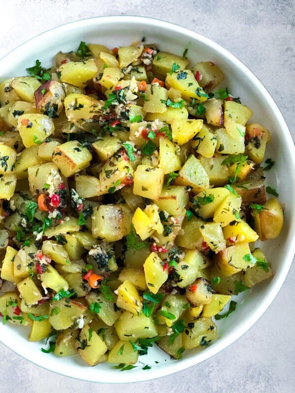 potato cubes friend with cilantro, galic and peppers. served on a plate.