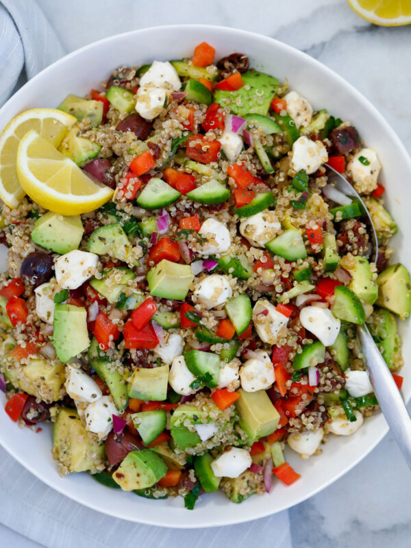 Mediterranean quinoa salad mixed up and served on a dish with a spoon and lemon wedges