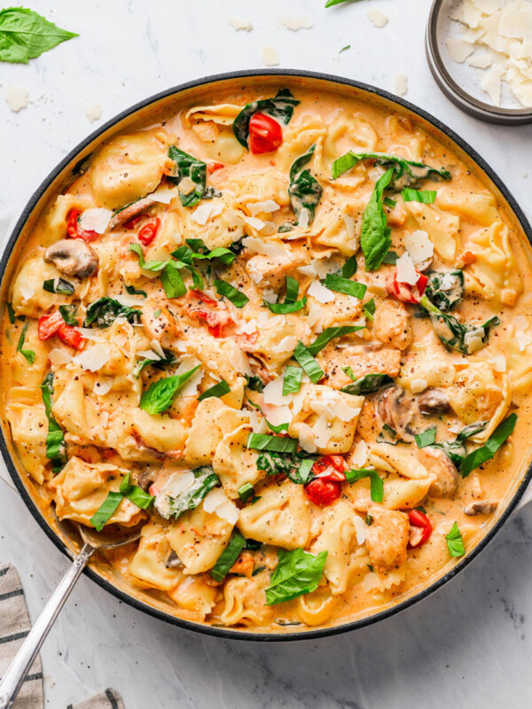 creamy-chicken-tortellini-pasta in a skillet, garnished with basil and shaved parmesan cheese
