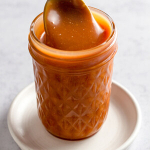 Close up of caramel sauce in a jar with a spoon.