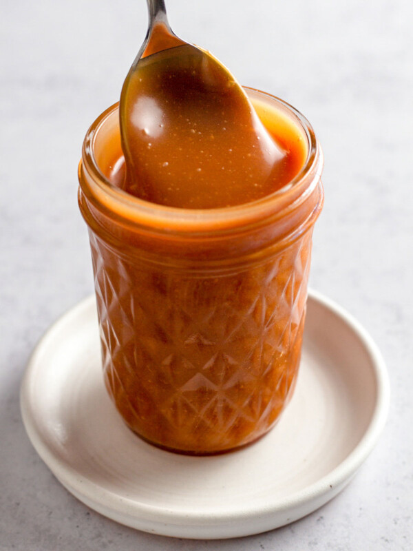 Close up of caramel sauce in a jar with a spoon.