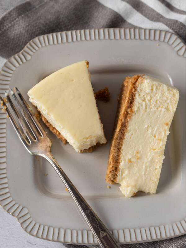 A slice of new york style cheesecake on a plate with the tip on the fork beside it.
