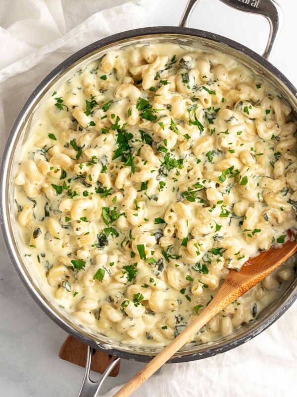 top down shot of spinach mac and cheese with wooden spoon in skillet