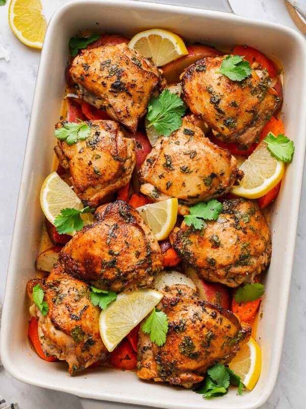 Chicken thighs in a baking dish with veggie and lemon wedges after baking