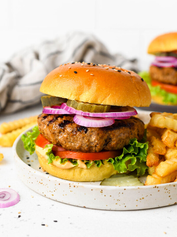 A homemade burger on a plate with toppings and fries.