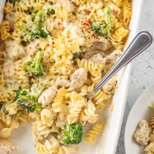 baked chicken and broccoli pasta in a white dish after baking with a spoon inside the dish