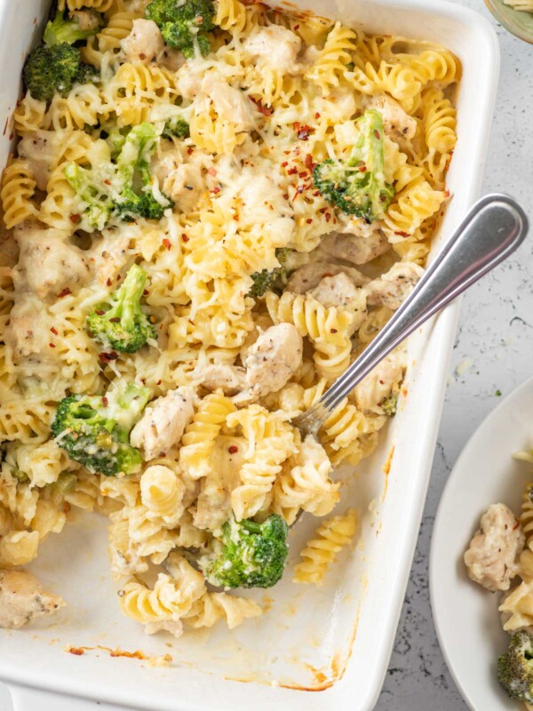 baked chicken and broccoli pasta in a white dish after baking with a spoon inside the dish