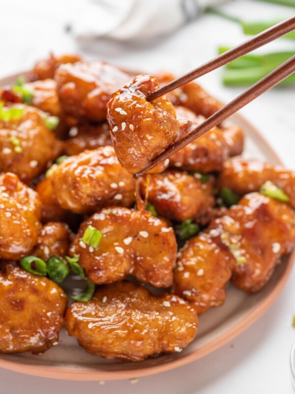 A plate with Crispy Honey Chicken with a pair of chopsticks lifting a piece up.