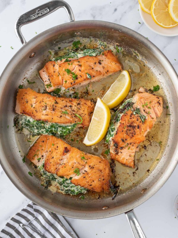 Overhead view of a pan of creamy stuffed spinach salmon with lemon wedges.