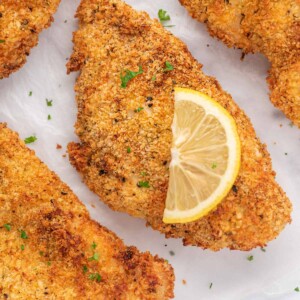Closeup of a crispy chicken cutlet with a lemon slice on top.