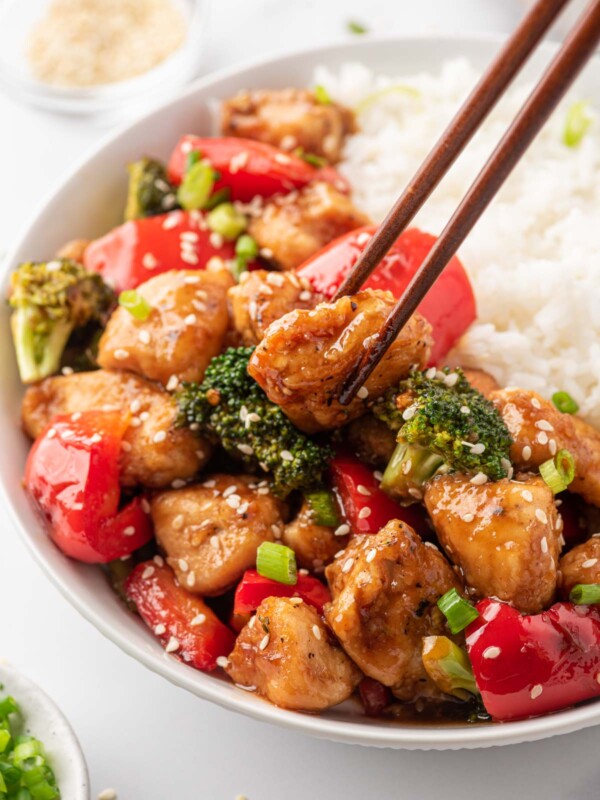 Chopsticks pick up a piece of Chicken Teriyaki Stir Fry from a bowl of rice.