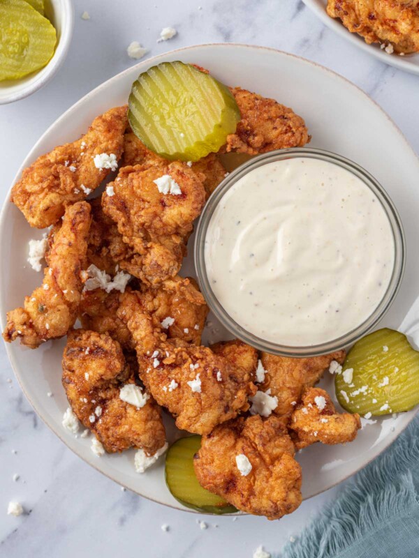 A plate of Nashville hot chicken tenders with pickles and dipping sauce.