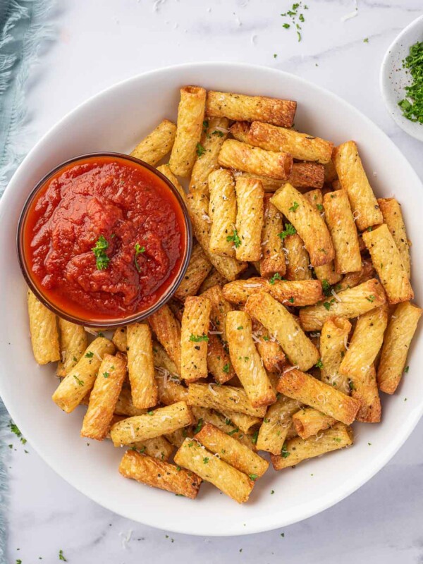 A plate of air fried pasta with a small bowl of marinara sauce.