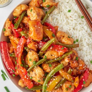 Sweet Thai chili chicken stir fry on a plate with rice and chopsticks.