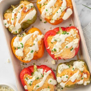 Healthy chicken stuffed peppers topped with ranch and crumbled blue cheese in a baking dish.