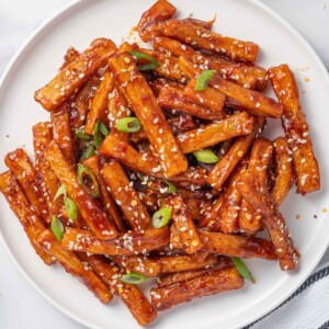 A plate of chilli fries topped with sesame seeds and green onions.