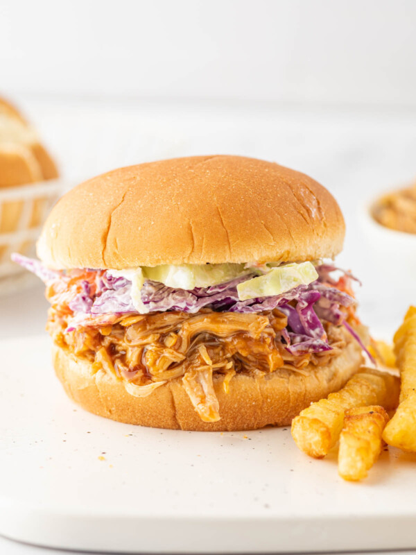 A bbq pulled chicken sandwich on a plate with french fries.