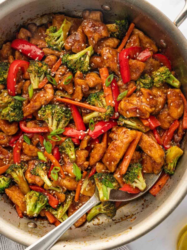 A spoon serve spicy hunan chicken from a skillet.
