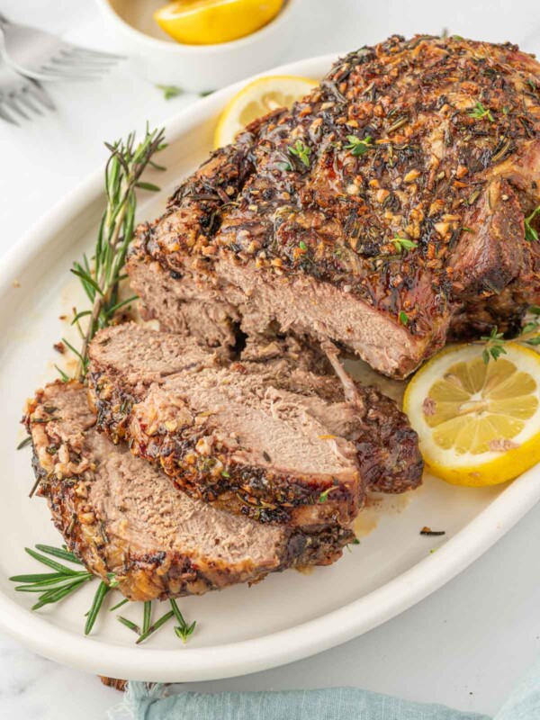 Leg of lamb with slices cut garnished with lemon and rosemary.