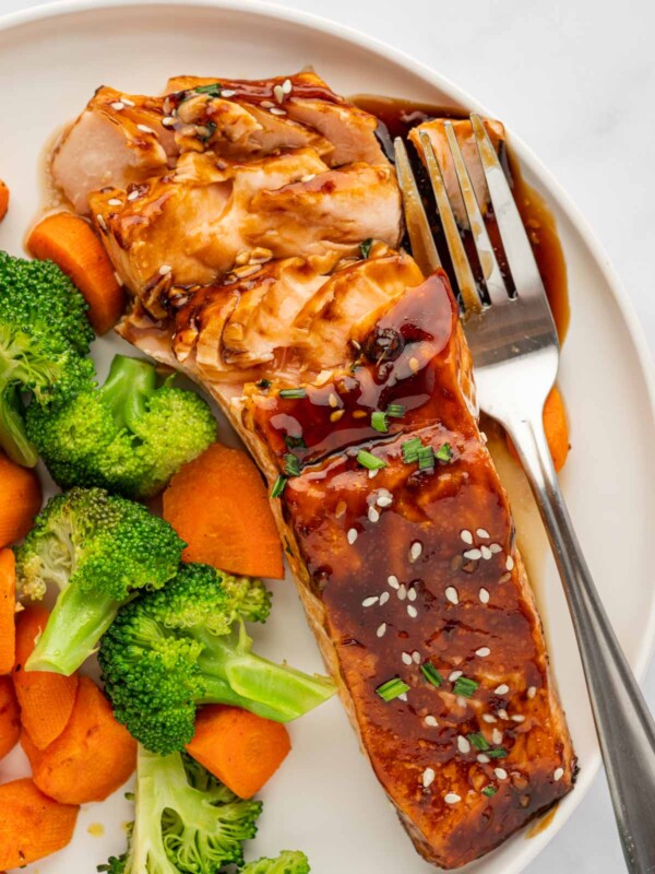 Teriyaki marinated salmon on a plate with veggies and a fork.