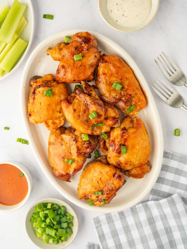 A platter of baked chicken thighs basted with buffalo sauce.