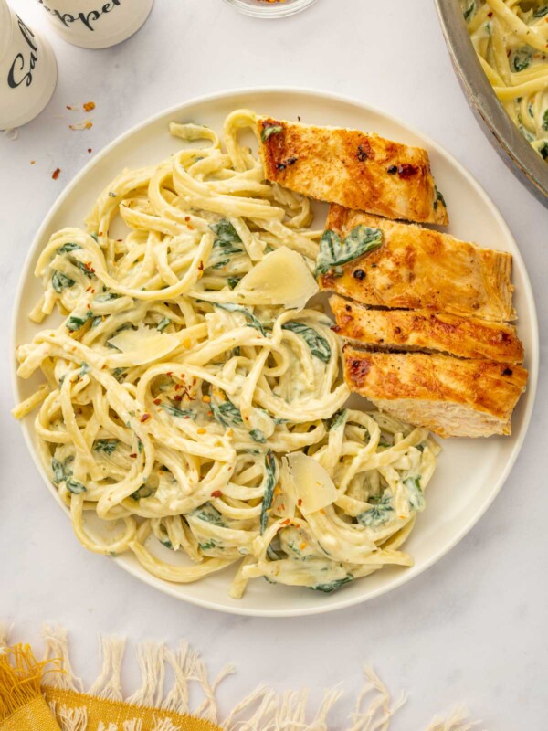 A plate of cheesy pasta served with sliced chicken breast.