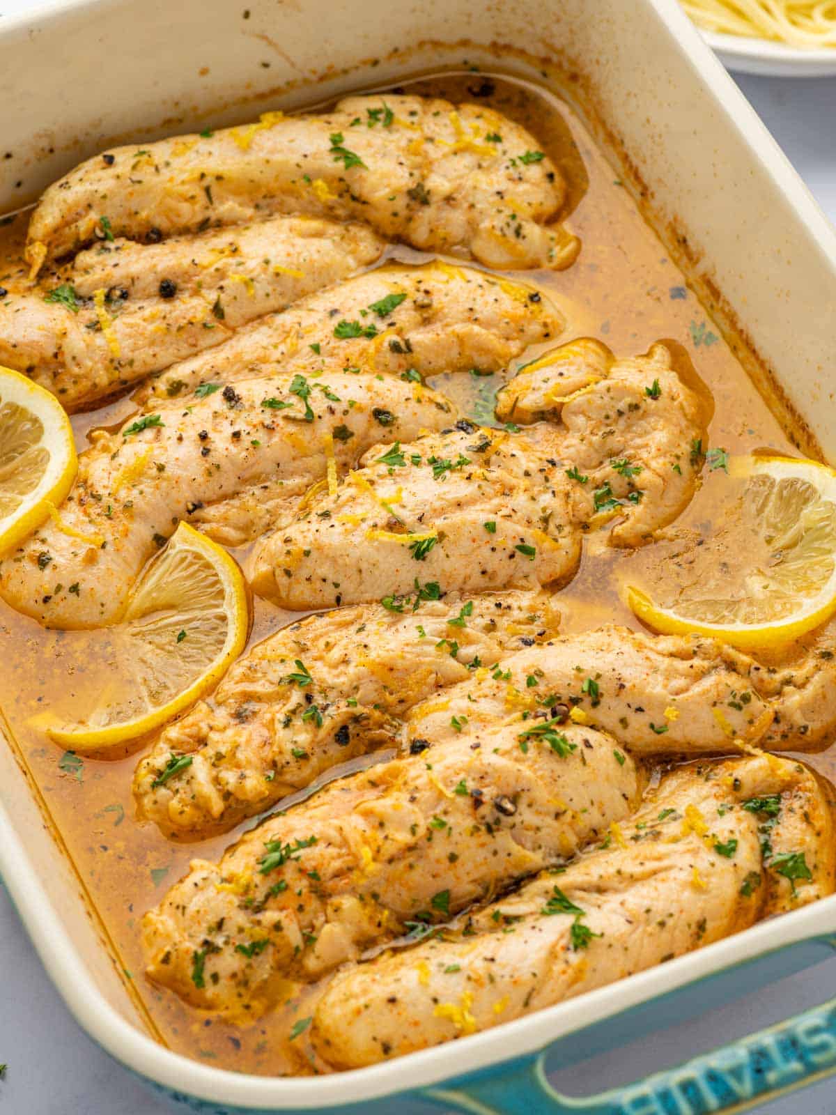 A baking dish with lemon pepper chicken tenders garnished with cilantro and lemon.