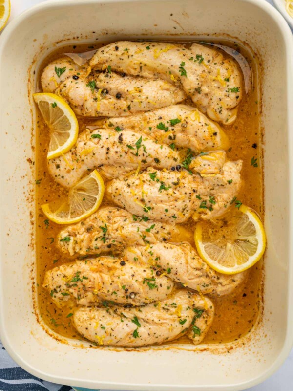 Lemon pepper chicken fingers baked in a dish and garnished with lemon.