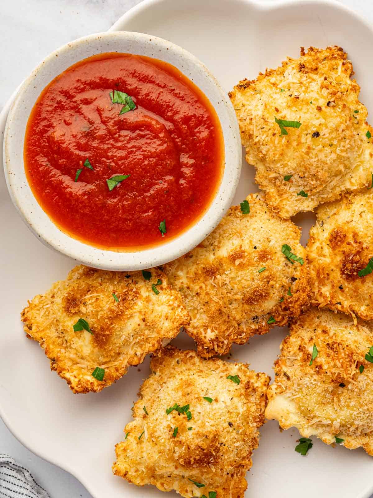 Air fried ravioli on a plate with a small bowl of marinara.