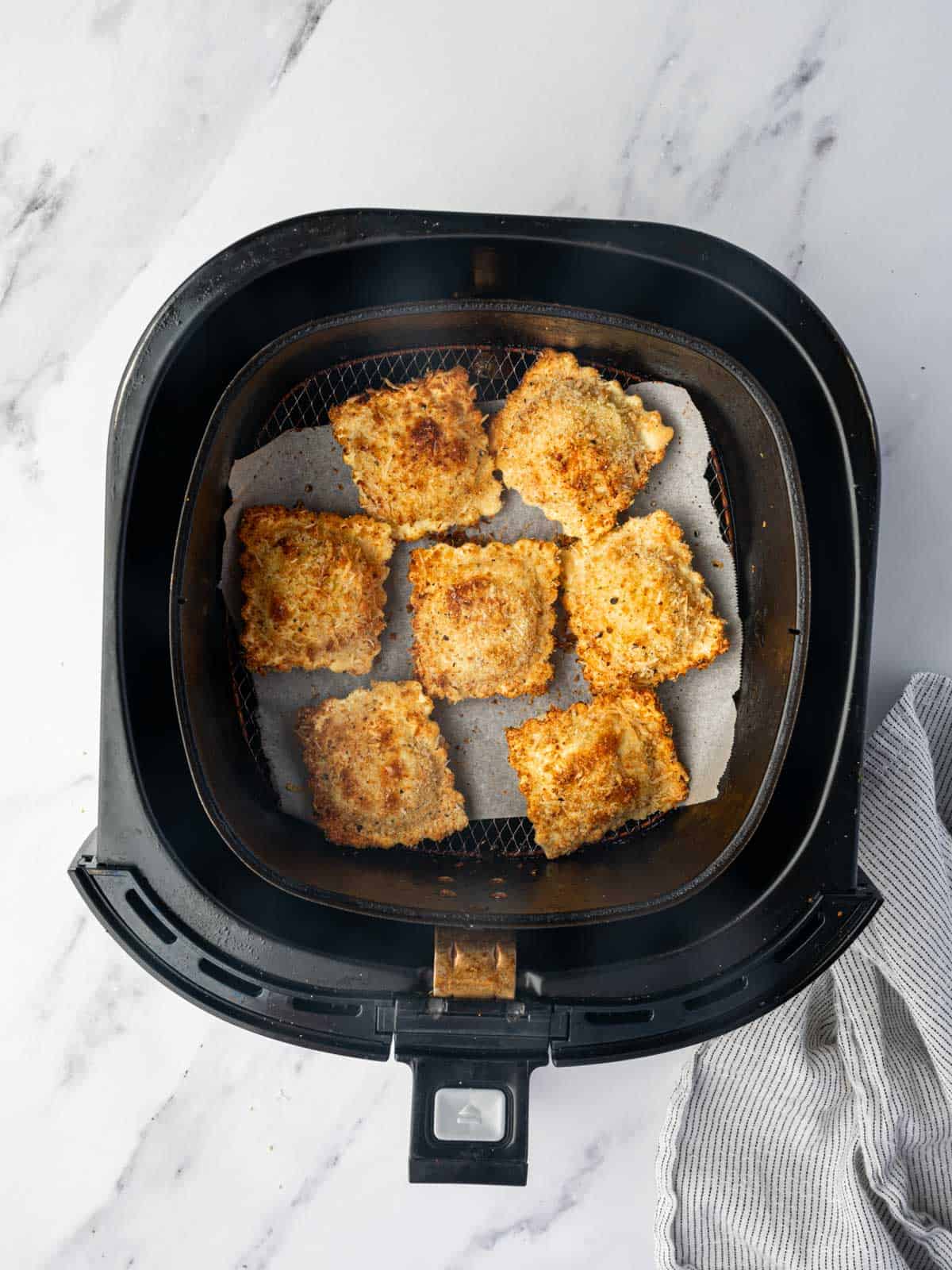 Air fryer basket with a single layer of air fried ravioli.