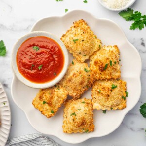 A platter of air fried ravioli with marinara sauce for dipping.