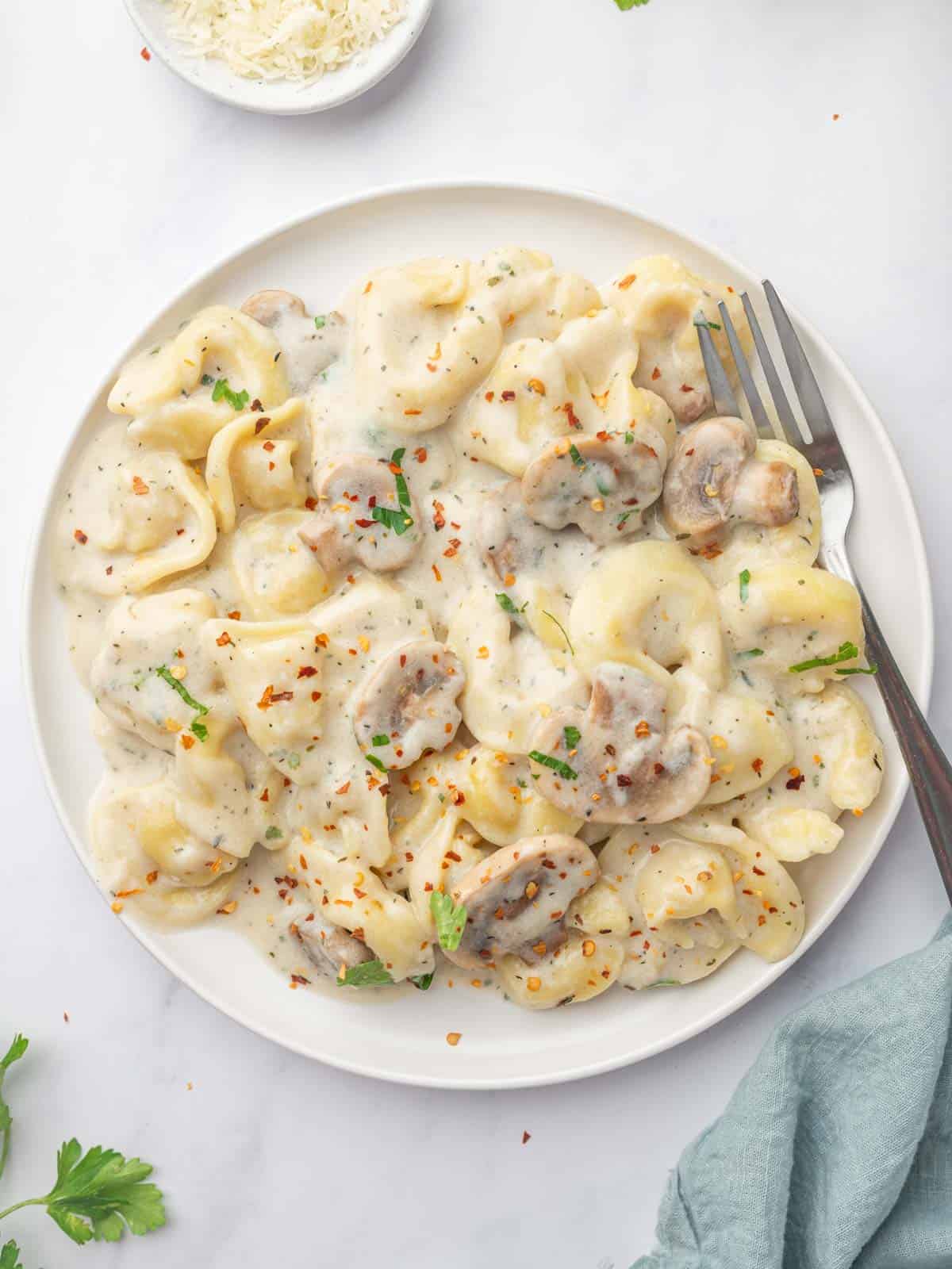 A fork rests on the side of a plate of cheese tortellini with alfredo sauce.