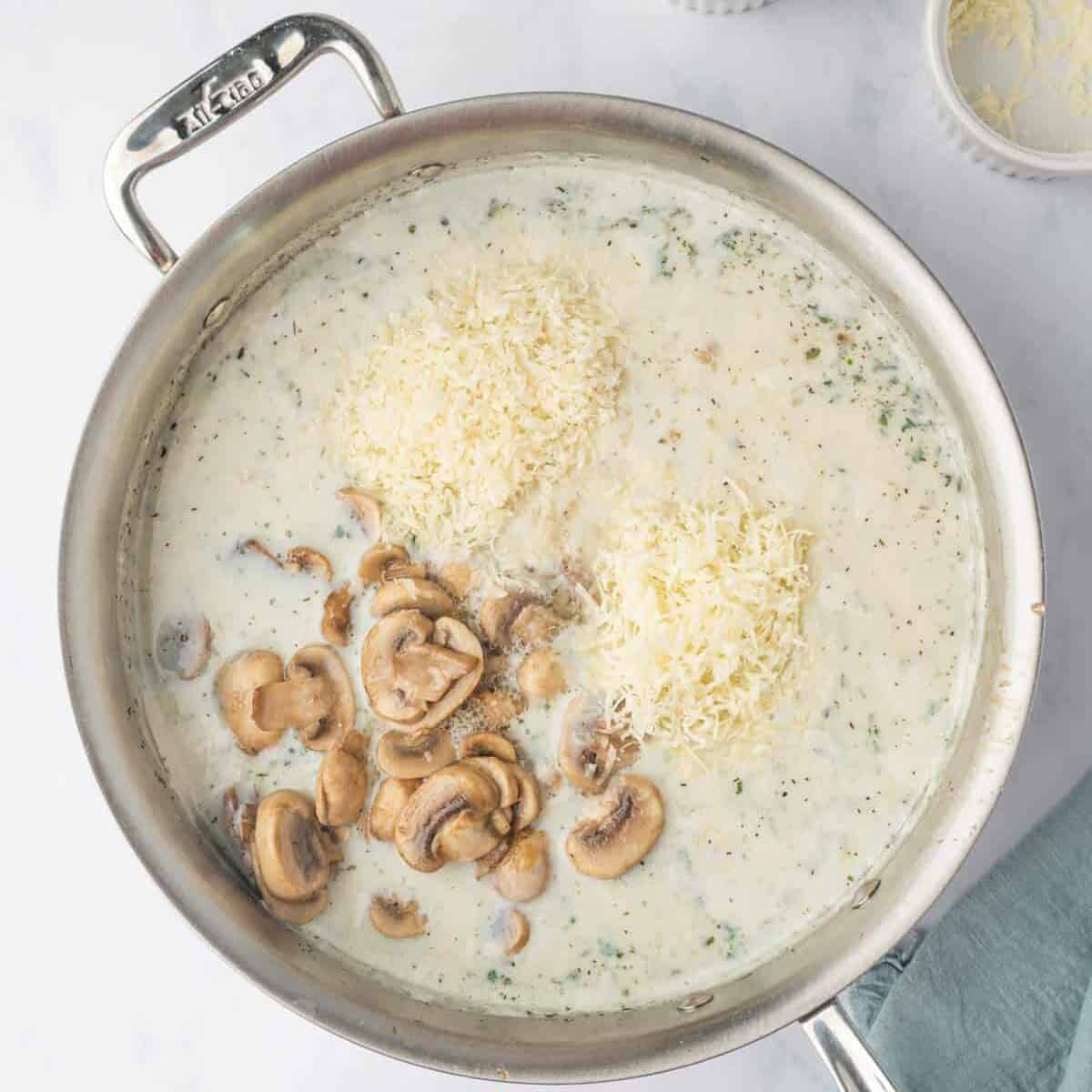 Alfredo sauce is combined with mushrooms and cheese in a skillet.