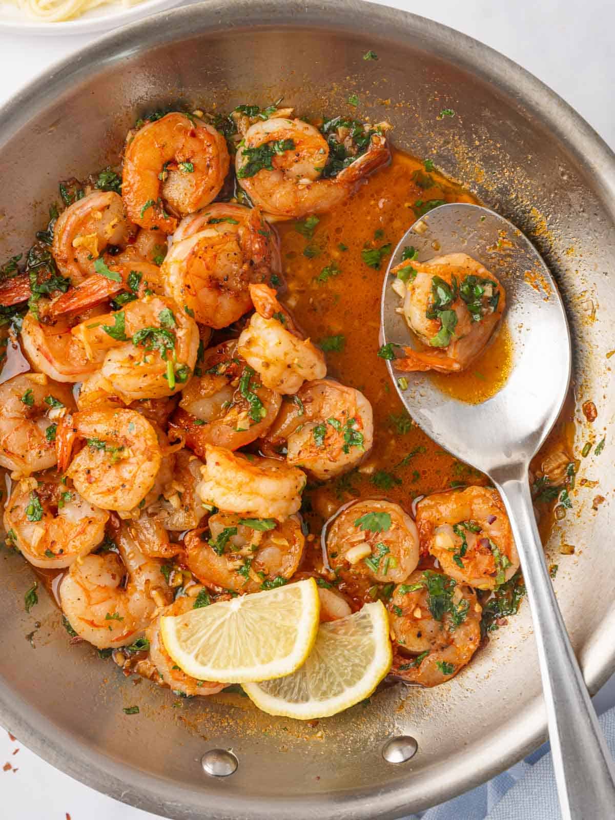 A spoon picks up a piece of spicy shrimp form a skillet.
