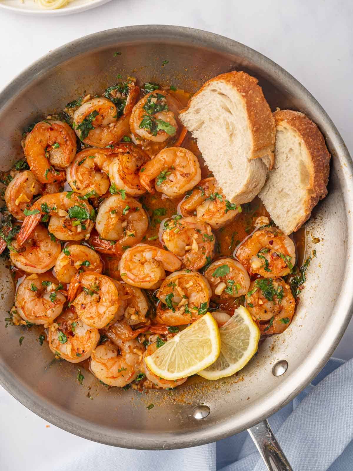 Shrimp scampi with spicy sauce in a skillet with bread and lemon slices.