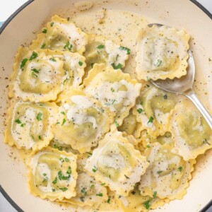 A spoon serves a piece of ravioli from a dutch oven.