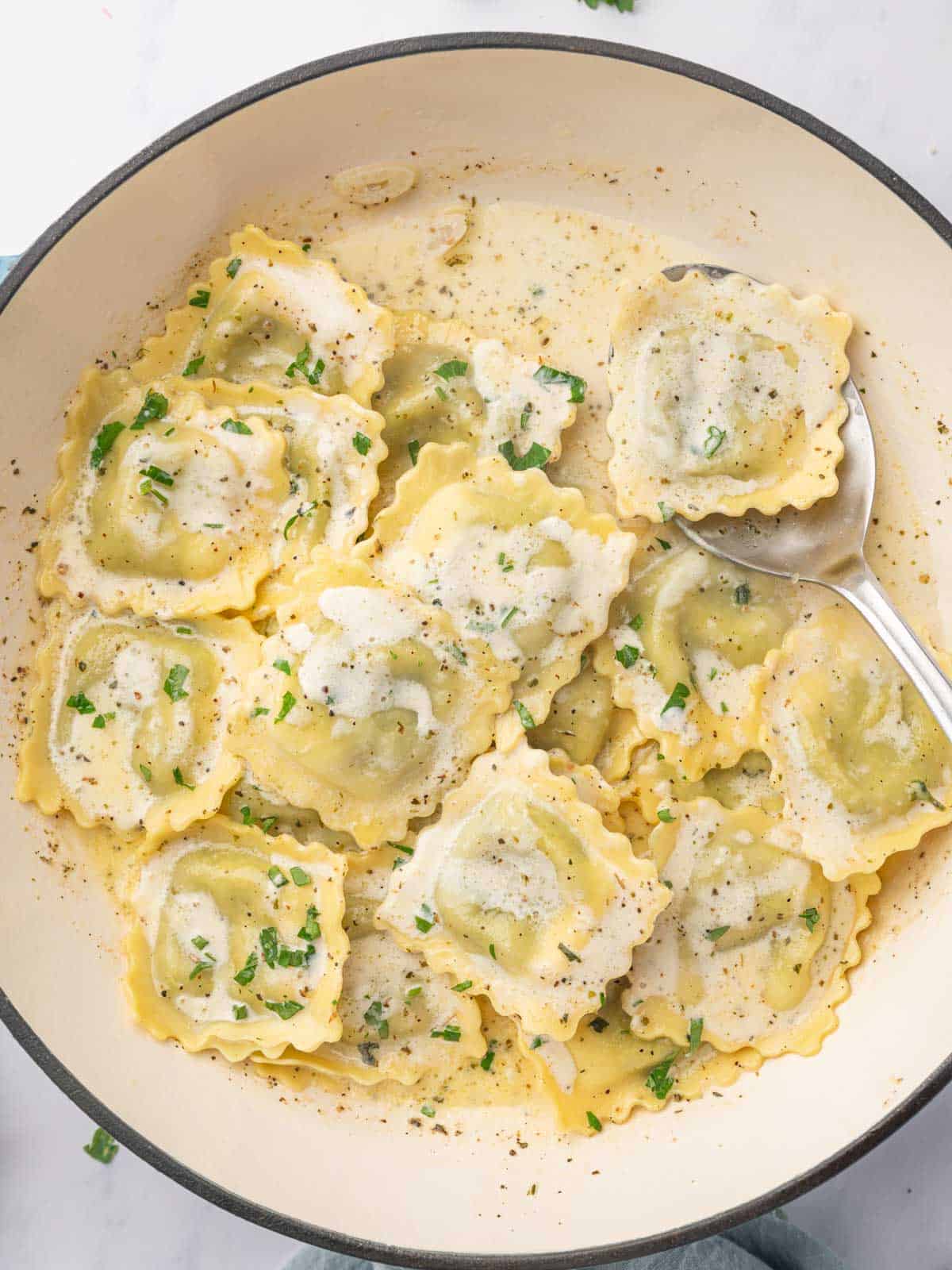 A spoon serves a piece of ravioli from a dutch oven.