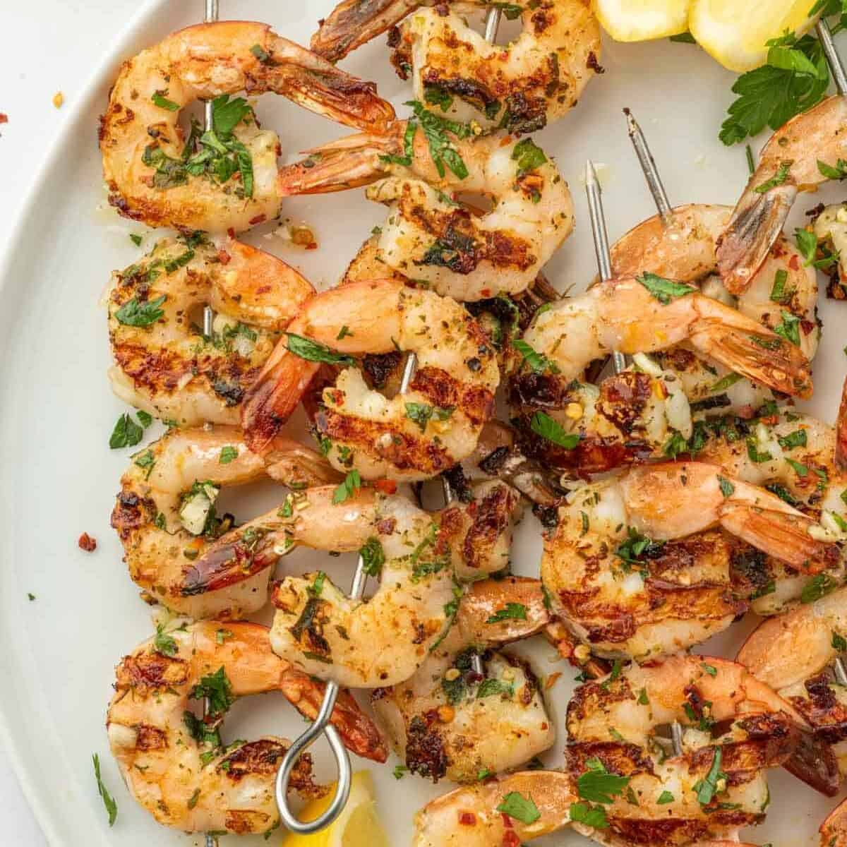 Shrimp kabobs with garlic on a white platter with lemon wedges.