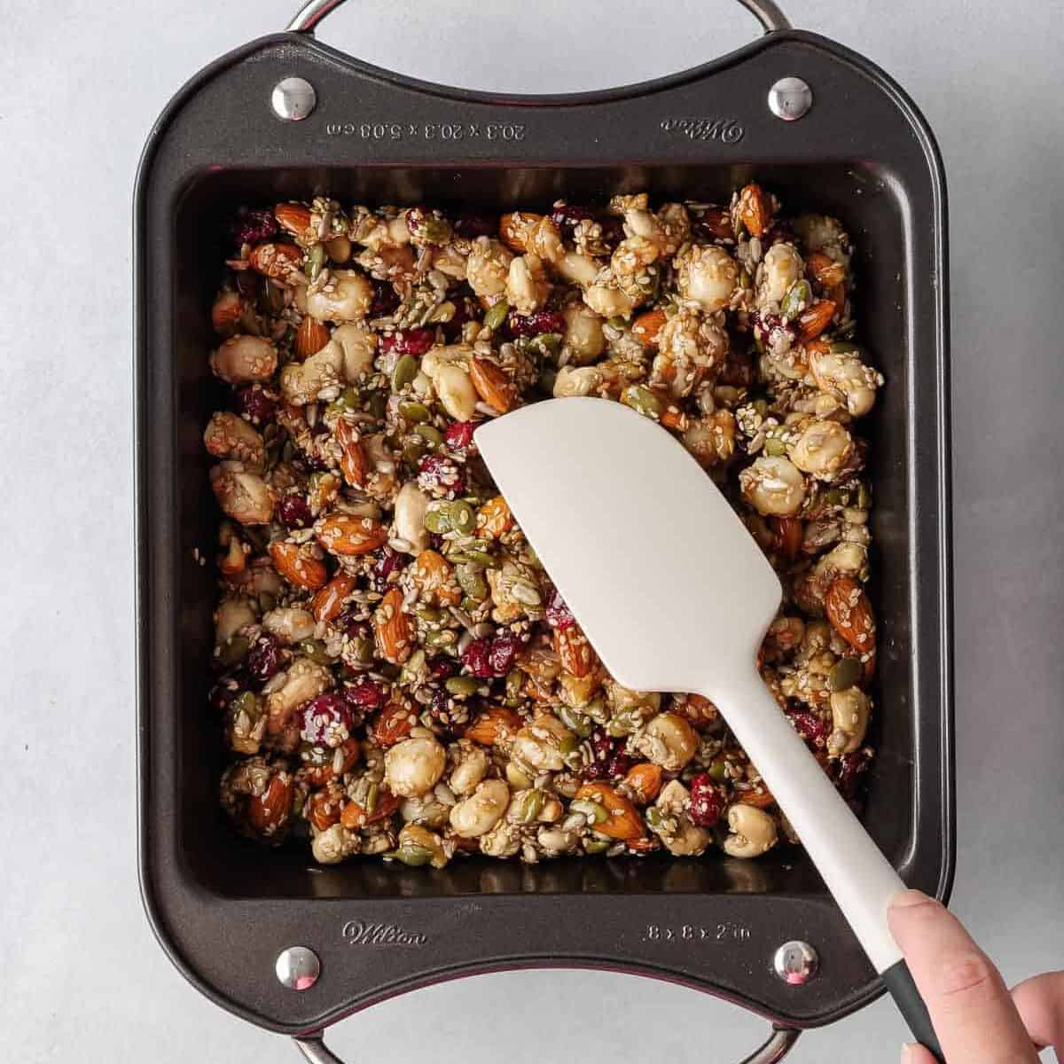 A spatula presses the healthy nut bar recipe into a pan.