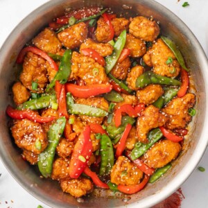 A skillet with sesame seed garnished chicken and vegetables.