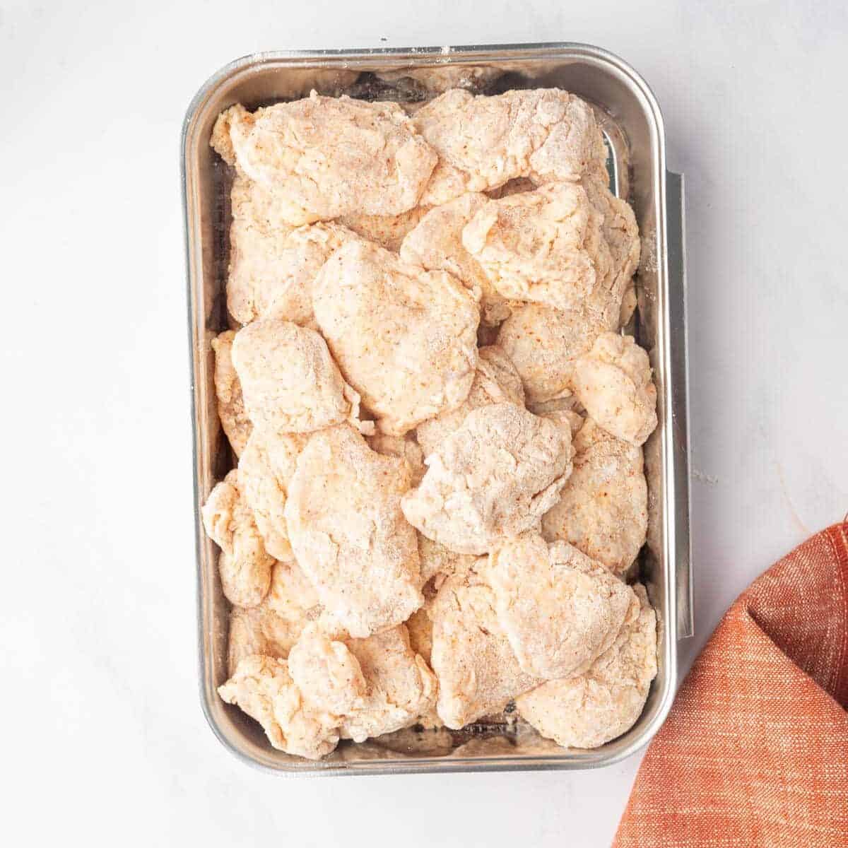 Flour coated chicken breast pieces on a tray.