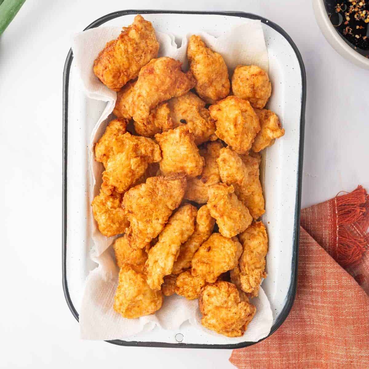 Fried chicken pieces drain on a paper towel on a tray.