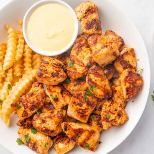 Grilled chicken nuggets on a plate with fries and dip.