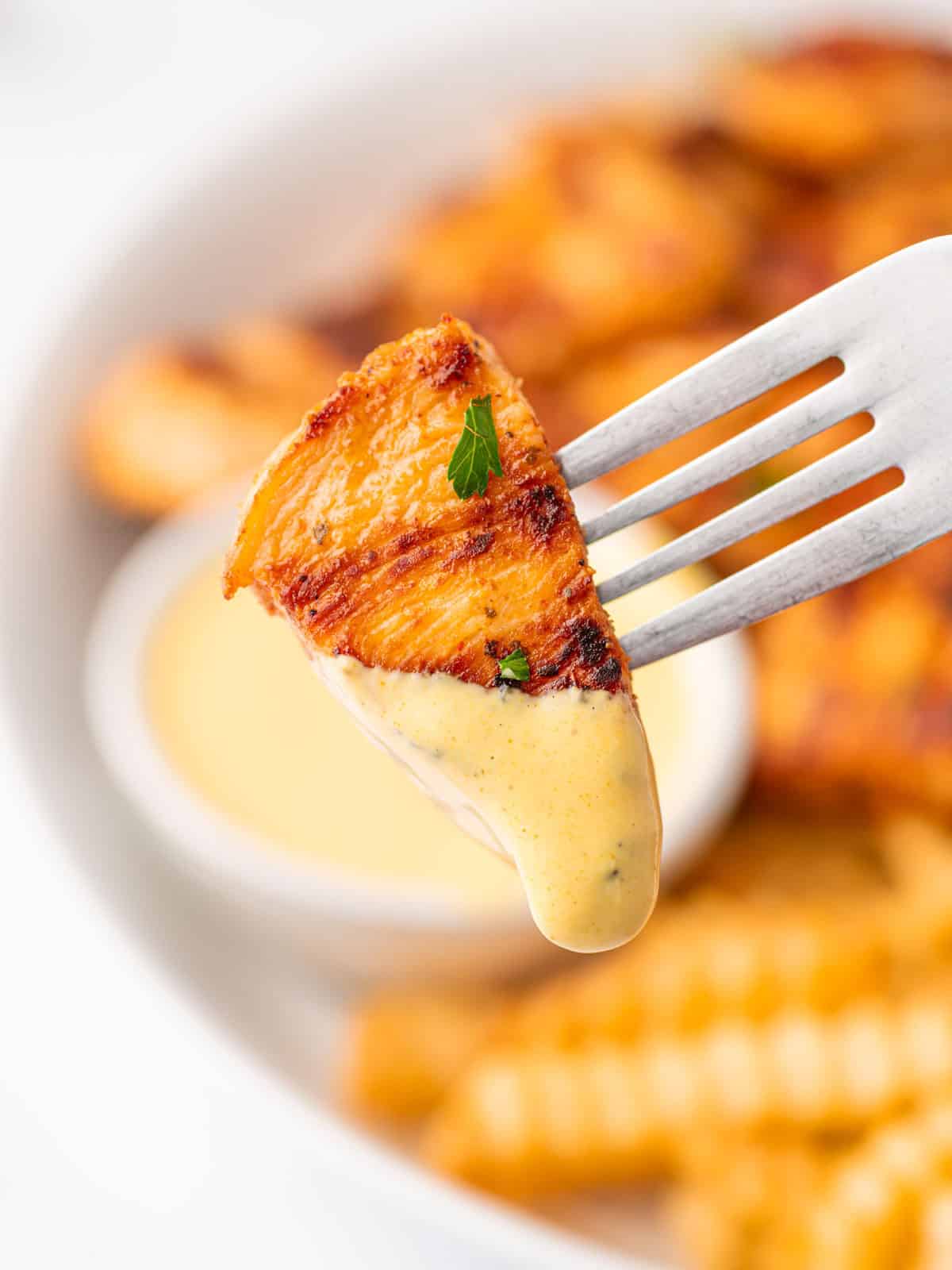 A grilled chicken nugget covered with dipping sauce is on a fork.